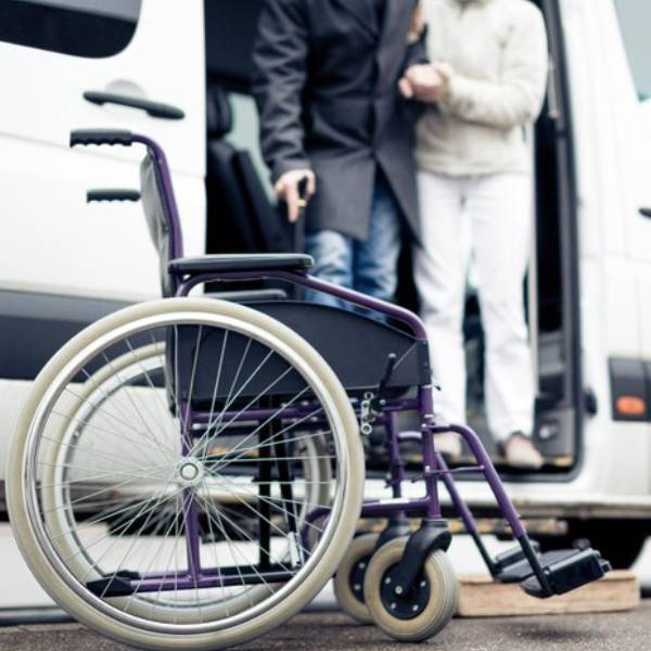 Empty wheelchair beside an accessible transport van with passengers